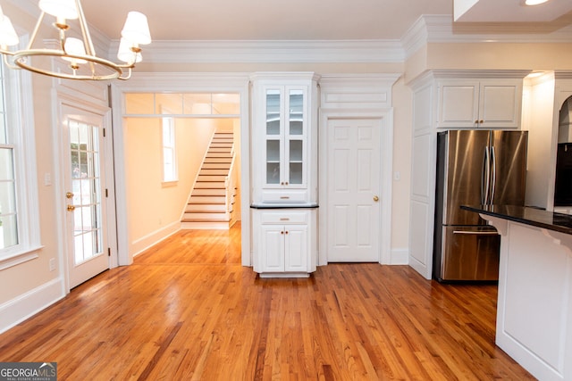 kitchen with white cabinets, ornamental molding, light hardwood / wood-style flooring, stainless steel refrigerator, and a notable chandelier