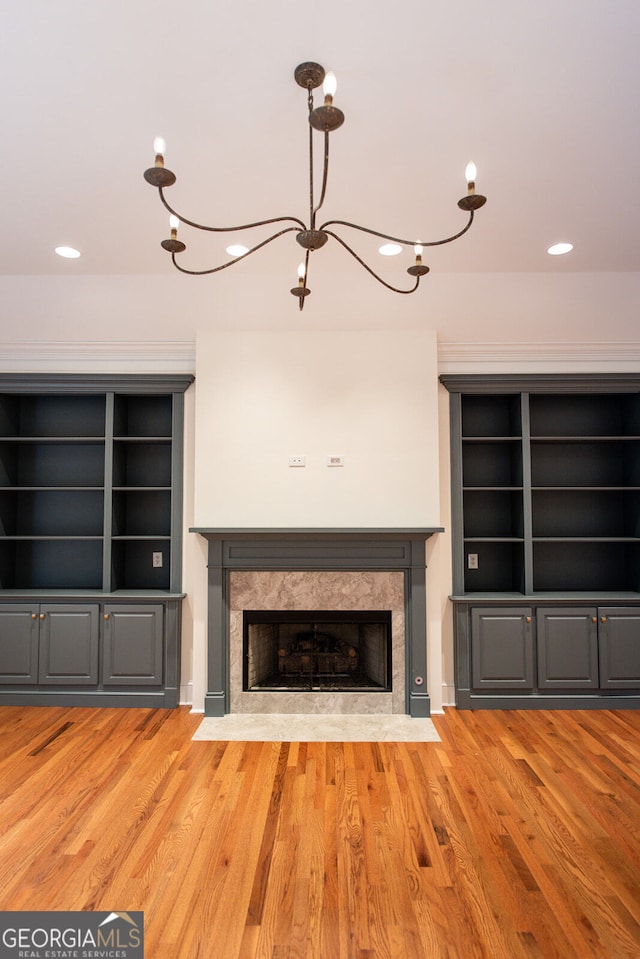 unfurnished living room with wood-type flooring, a high end fireplace, a chandelier, and built in shelves