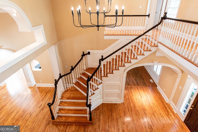 stairs with a notable chandelier, a wealth of natural light, a high ceiling, and hardwood / wood-style flooring