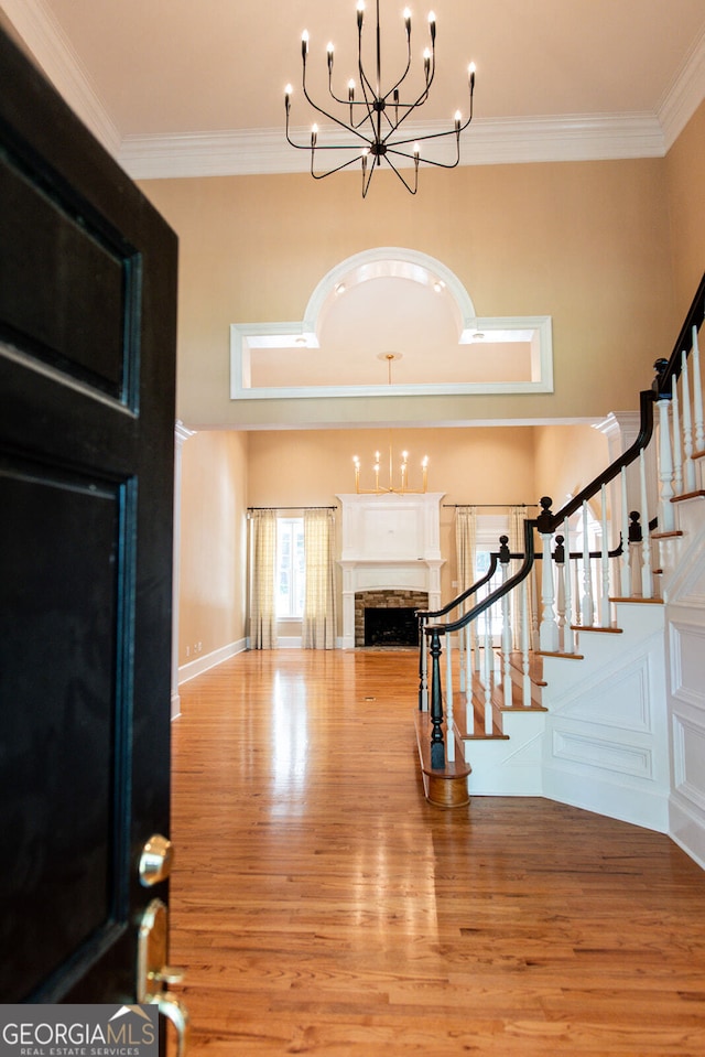 foyer entrance featuring ornamental molding, light hardwood / wood-style floors, an inviting chandelier, and a stone fireplace