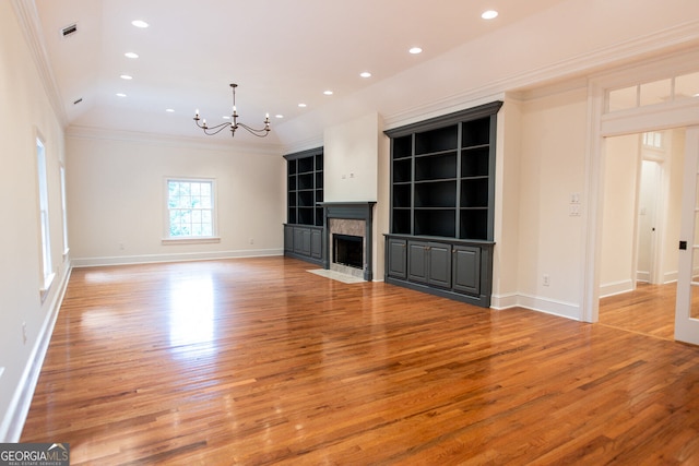 unfurnished living room with a fireplace, light wood-type flooring, ornamental molding, and a chandelier