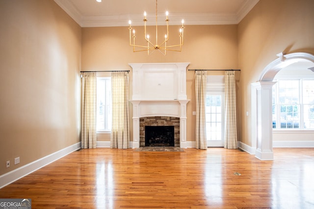 unfurnished living room with crown molding, a stone fireplace, an inviting chandelier, and light hardwood / wood-style flooring