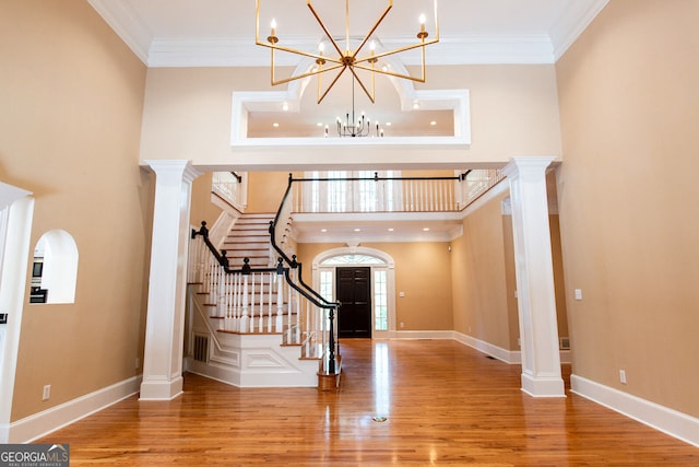 foyer entrance with wood-type flooring, decorative columns, ornamental molding, and an inviting chandelier