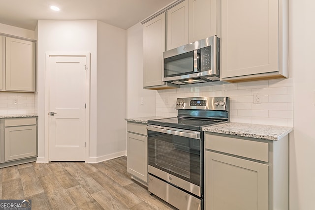 kitchen with light stone counters, stainless steel appliances, light wood-type flooring, and gray cabinetry