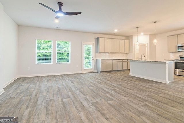 kitchen with ceiling fan, an island with sink, sink, stainless steel appliances, and light hardwood / wood-style floors