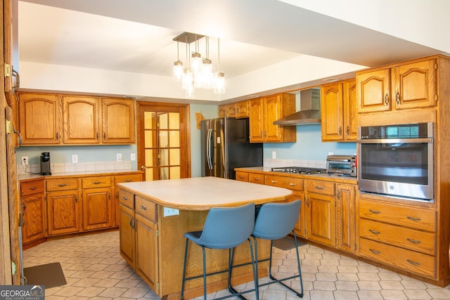 kitchen featuring stainless steel appliances, a center island, decorative light fixtures, wall chimney range hood, and a chandelier