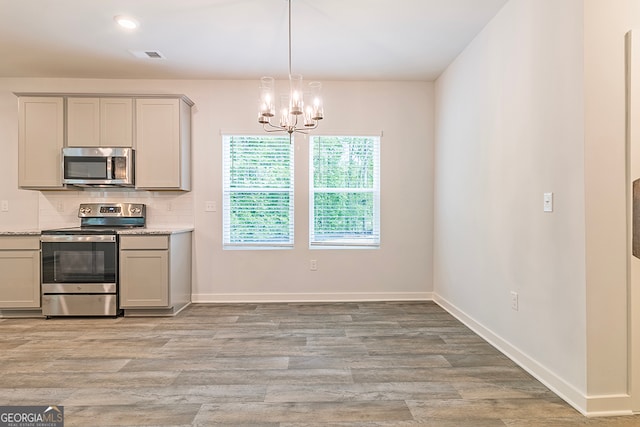 kitchen with gray cabinetry, light hardwood / wood-style floors, stainless steel appliances, and a notable chandelier