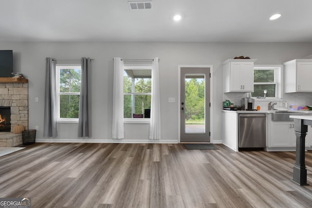 kitchen with light wood-type flooring, a stone fireplace, white cabinetry, and dishwasher