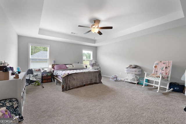 carpeted bedroom with multiple windows, a tray ceiling, and ceiling fan