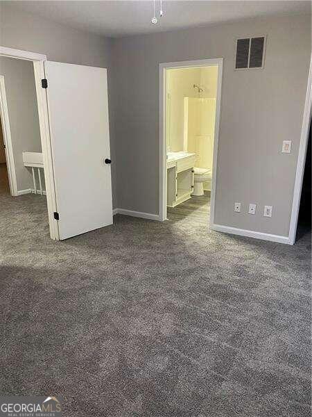 unfurnished bedroom with connected bathroom and dark colored carpet