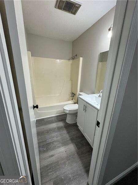 full bathroom with vanity, a textured ceiling, hardwood / wood-style flooring, bathing tub / shower combination, and toilet