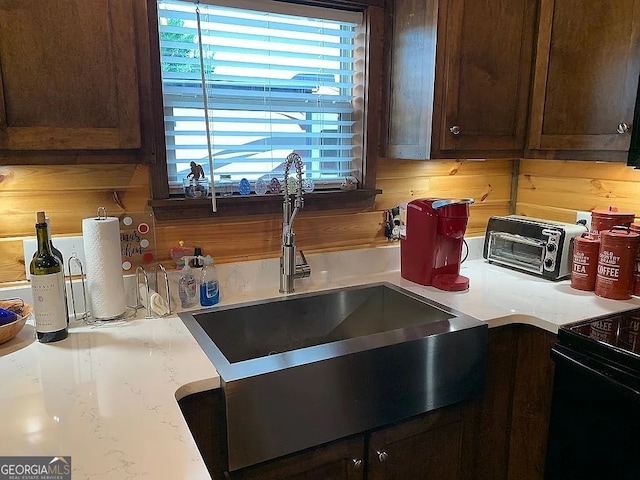 kitchen with wooden walls, black range with electric stovetop, dark brown cabinetry, and sink