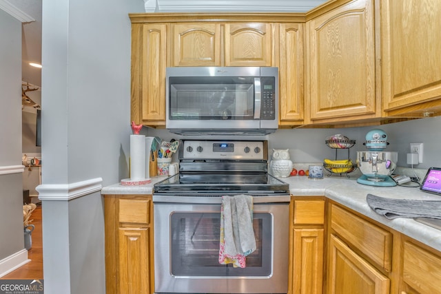 kitchen featuring appliances with stainless steel finishes, wood-type flooring, and crown molding