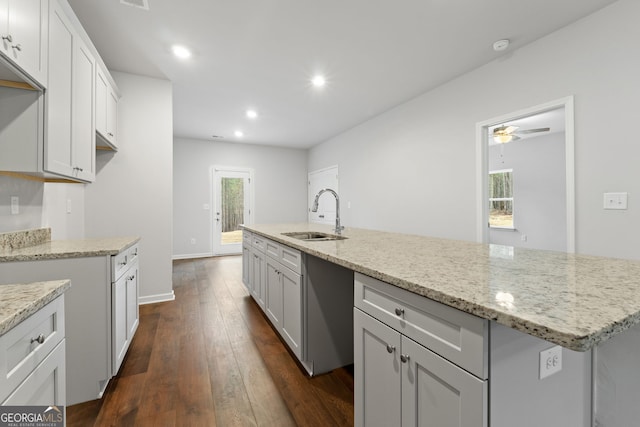 kitchen featuring a center island with sink, sink, ceiling fan, light stone counters, and dark hardwood / wood-style flooring