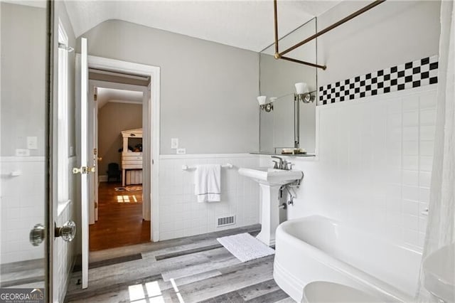 bathroom with wood-type flooring, shower / tub combo with curtain, tile walls, and vaulted ceiling