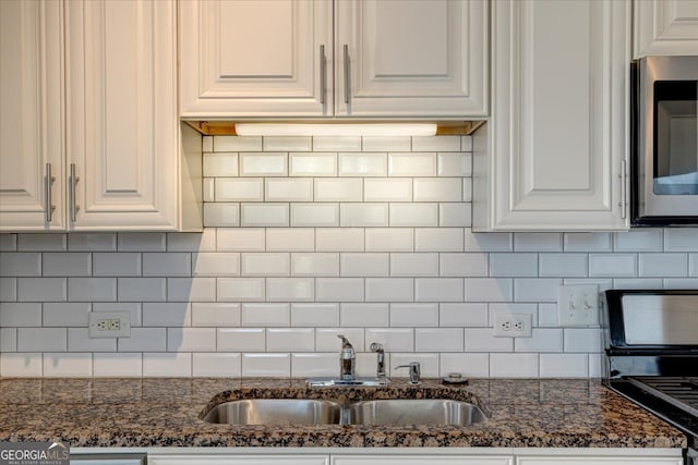 kitchen featuring decorative backsplash, dark stone countertops, white cabinets, and sink