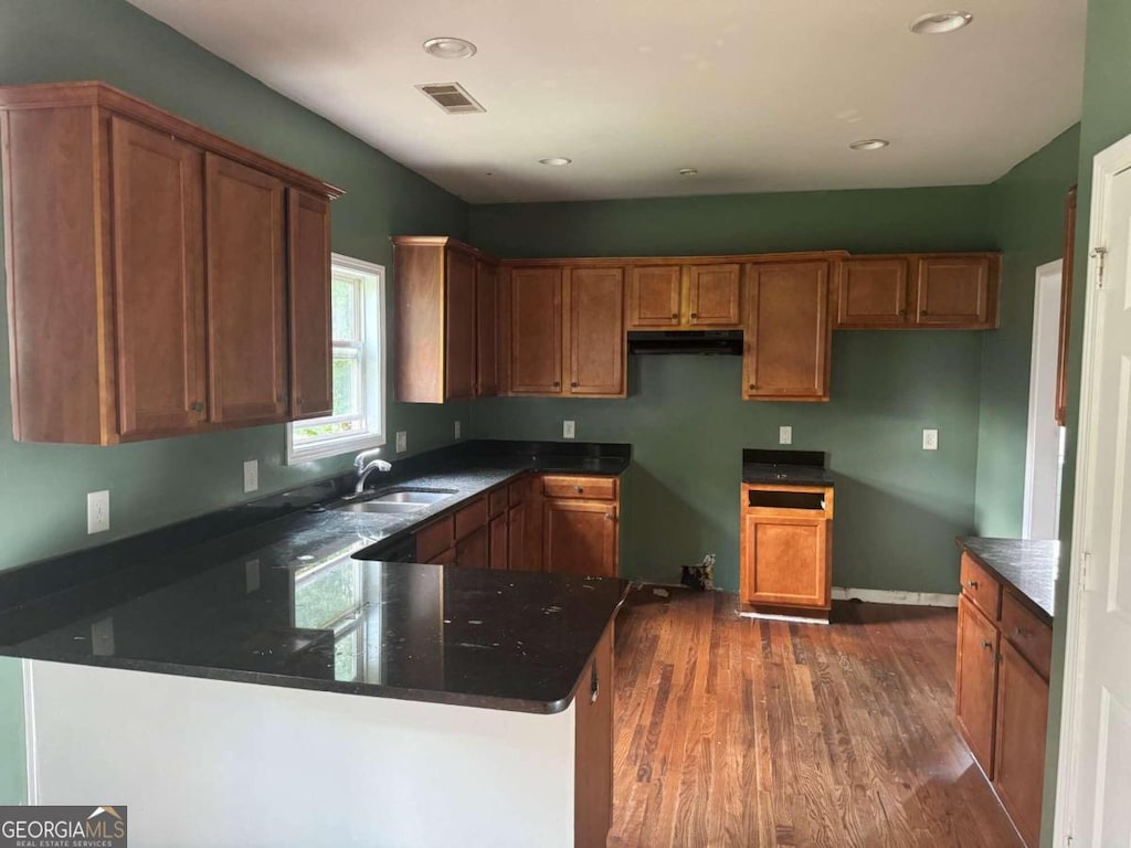 kitchen featuring kitchen peninsula, hardwood / wood-style floors, dark stone countertops, and sink