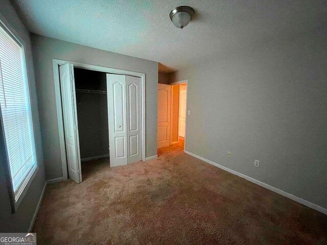 unfurnished bedroom featuring carpet floors, a textured ceiling, and a closet