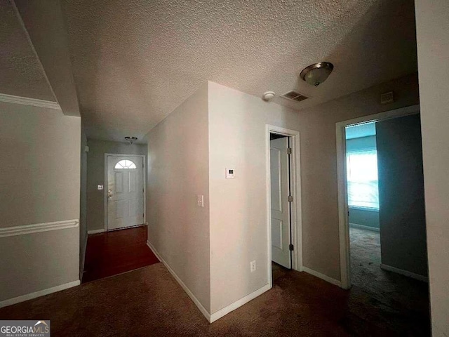 corridor with dark carpet and a textured ceiling