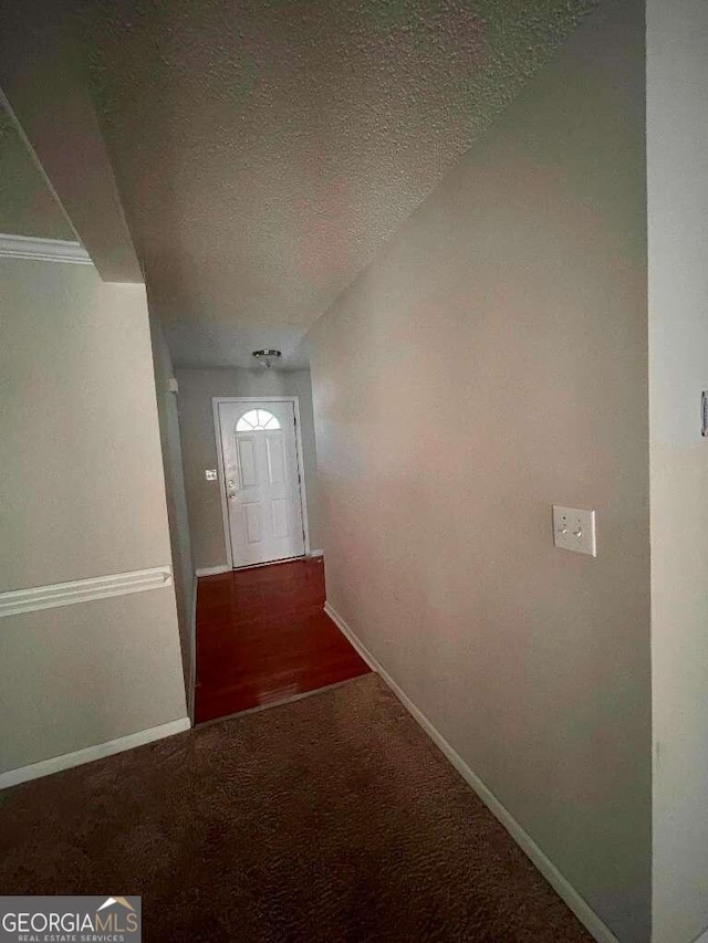 hallway with dark colored carpet and a textured ceiling