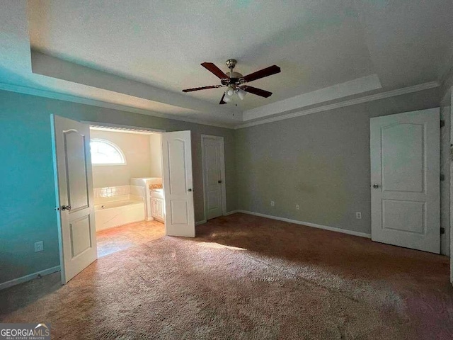 unfurnished bedroom with a tray ceiling, carpet floors, ensuite bathroom, crown molding, and ceiling fan