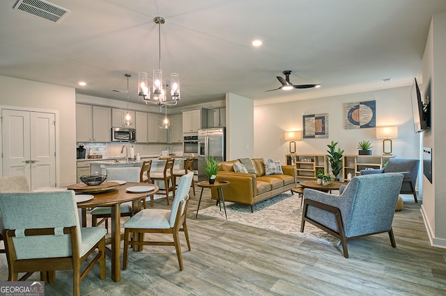 living room featuring light wood-type flooring, ceiling fan with notable chandelier, and sink