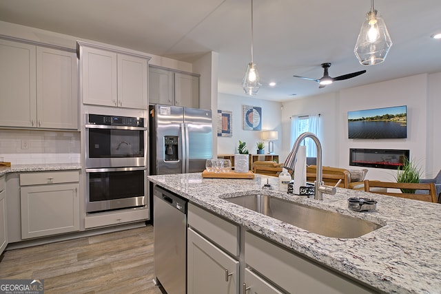 kitchen with ceiling fan, gray cabinets, appliances with stainless steel finishes, light hardwood / wood-style floors, and decorative backsplash