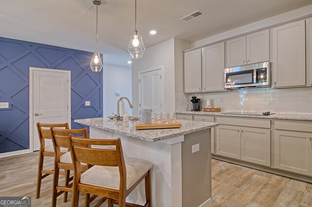 kitchen featuring black electric stovetop, light hardwood / wood-style floors, a kitchen breakfast bar, a center island with sink, and decorative light fixtures