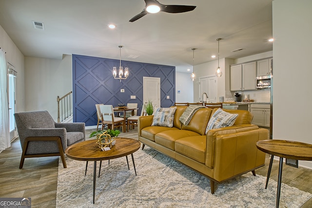 living room with ceiling fan with notable chandelier and light hardwood / wood-style floors