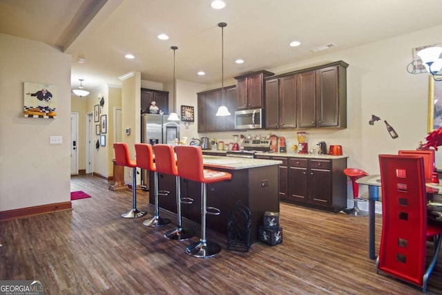 kitchen featuring pendant lighting, a kitchen island with sink, stainless steel appliances, a kitchen breakfast bar, and dark hardwood / wood-style flooring