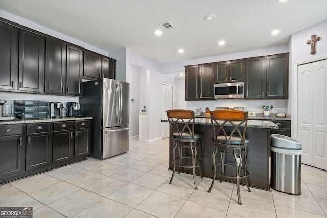 kitchen with appliances with stainless steel finishes, light tile patterned floors, a kitchen island, and stone counters