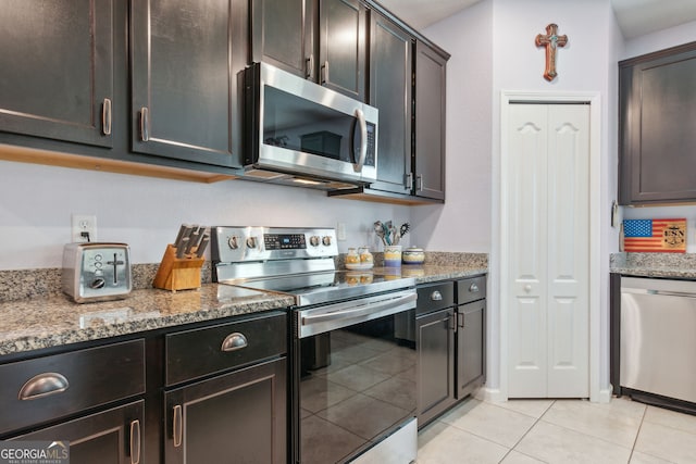 kitchen featuring light stone countertops, dark brown cabinets, light tile patterned floors, and stainless steel appliances