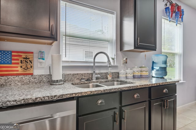 kitchen featuring stainless steel dishwasher, sink, light tile patterned floors, and light stone counters