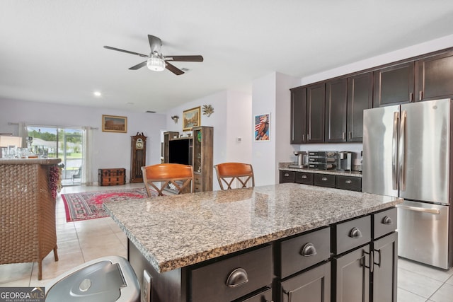 kitchen with stainless steel refrigerator, a kitchen island, light stone countertops, light tile patterned floors, and ceiling fan