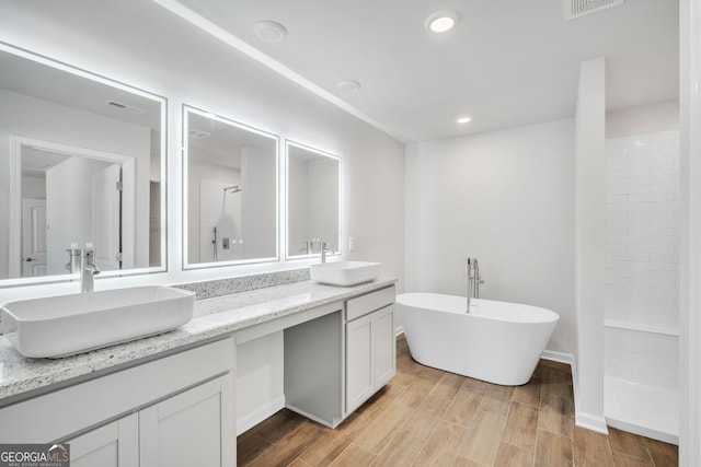 full bathroom featuring double vanity, tiled shower, a sink, and wood finish floors