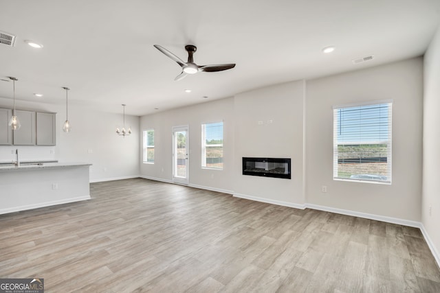 unfurnished living room with light wood finished floors, recessed lighting, visible vents, a glass covered fireplace, and ceiling fan with notable chandelier