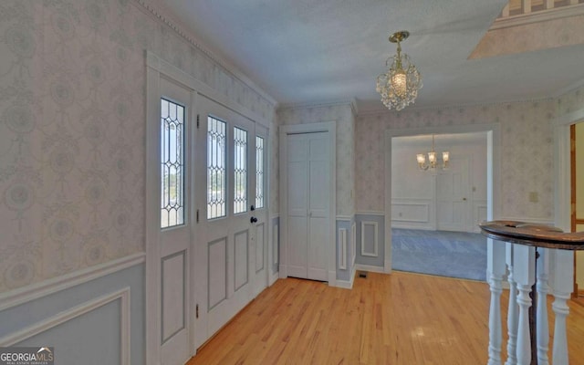 entrance foyer featuring light wood-type flooring, ornamental molding, and a chandelier