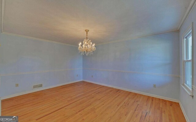 spare room with a chandelier, light hardwood / wood-style floors, and crown molding