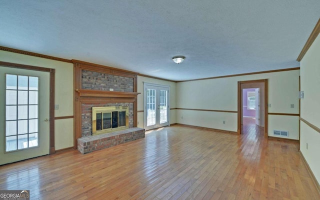 unfurnished living room with a brick fireplace, a textured ceiling, light wood-type flooring, and plenty of natural light