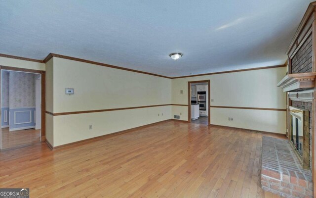 unfurnished living room featuring ornamental molding, light wood-type flooring, a textured ceiling, and a fireplace