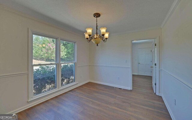 unfurnished room featuring a textured ceiling, crown molding, dark hardwood / wood-style flooring, and a chandelier