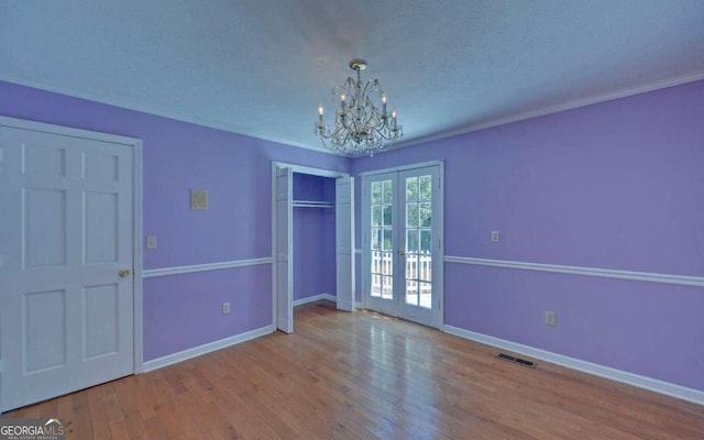 spare room with a textured ceiling, hardwood / wood-style floors, french doors, and a notable chandelier