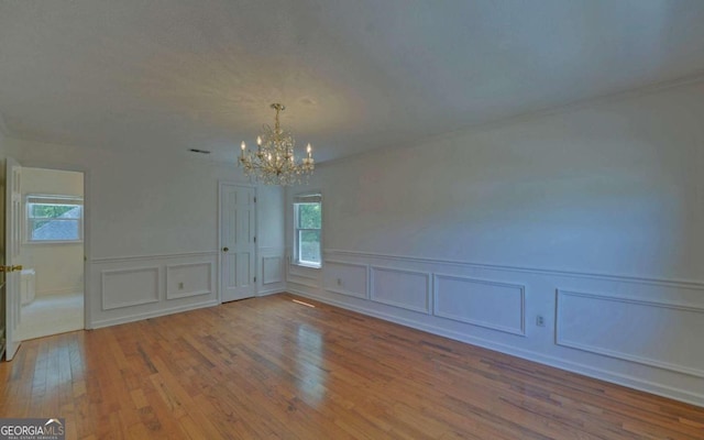 spare room with a notable chandelier, a wealth of natural light, and hardwood / wood-style flooring