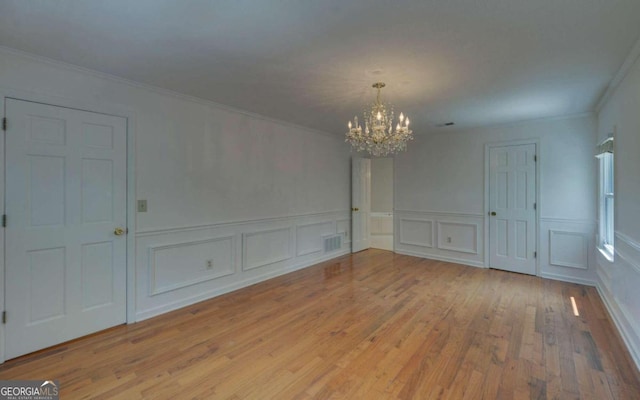 empty room featuring an inviting chandelier, light hardwood / wood-style floors, and ornamental molding