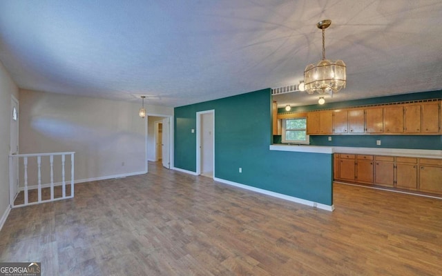 kitchen featuring an inviting chandelier, light wood-type flooring, a textured ceiling, and decorative light fixtures