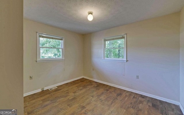 empty room featuring a textured ceiling, plenty of natural light, and dark hardwood / wood-style flooring