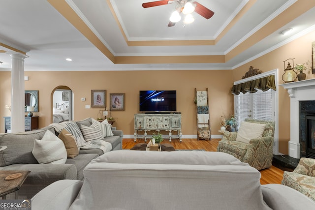 living room with light wood-type flooring, decorative columns, a premium fireplace, crown molding, and ceiling fan