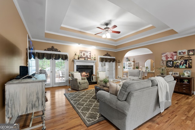 living room featuring light hardwood / wood-style flooring, a tray ceiling, ceiling fan, and a premium fireplace