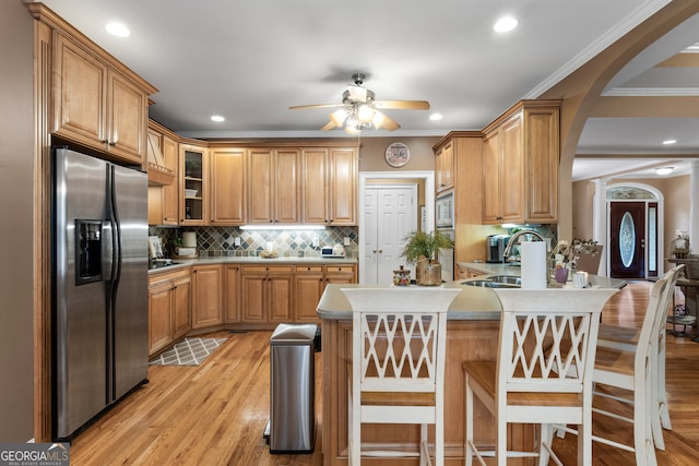 kitchen with ceiling fan, appliances with stainless steel finishes, a breakfast bar area, crown molding, and light hardwood / wood-style floors