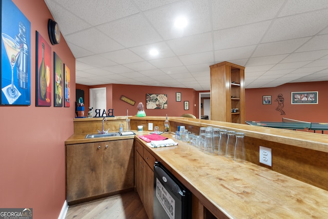 bar featuring sink, light hardwood / wood-style flooring, a drop ceiling, butcher block countertops, and stainless steel dishwasher